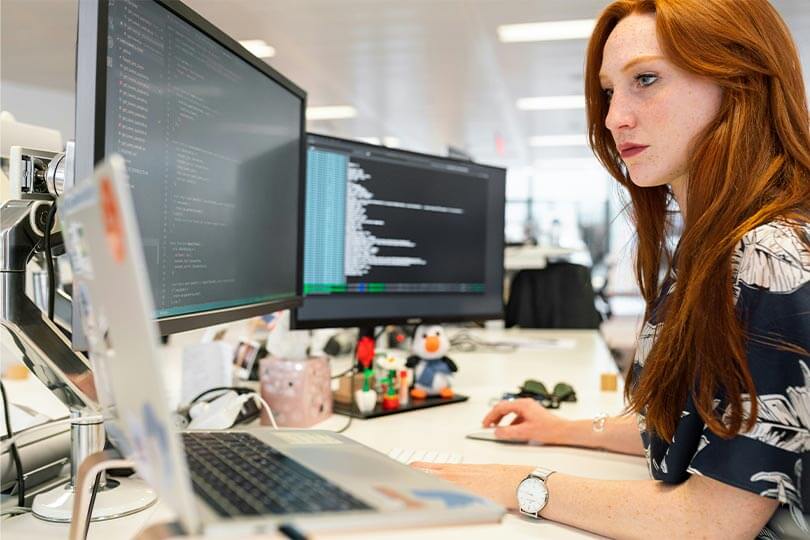 Female engineer coding at multi-monitor workstation. With IBM TLS data erasure, end user device erasures can be launched automatically based on policy. Photo by ThisisEngineering RAEng at Unsplash.