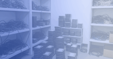 Disorganized IT storage room with shelves and stacks of hard drives awaiting secure decommissioning by an ITAD provider.